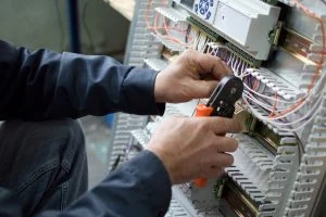 A person uses a tool to work on wiring in an electrical panel, ensuring everything is set up safely for a furnace installation in Brampton, Water Heater Services, brampton furnace repair