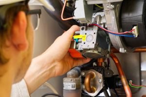 A technician carefully adjusts wiring on a machine with various colored wires and metallic components, focusing on a small device marked with "CO2," ensuring safe operations while recalling essential furnace installation tips