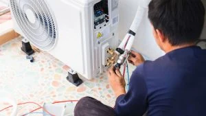 A technician expertly installs or repairs an outdoor air conditioning unit on a tiled surface, ensuring seamless operation. Whether it's cooling systems or furnace repair in Mississauga, professional service is just a call away, furnace replacement ontario