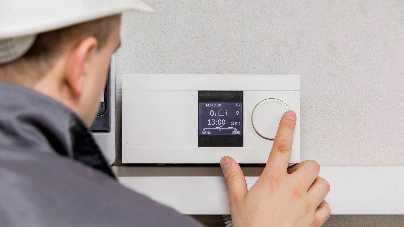 A man in a hard hat is pointing at a thermostat.