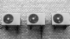 Three air conditioning units, expertly installed by an HVAC company, are mounted on a brick wall in a neat row, Install AC