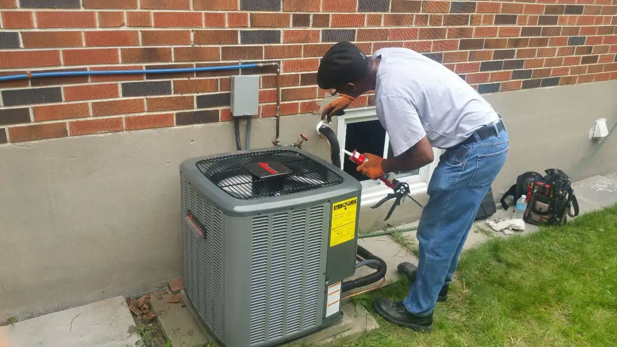 An HVAC technician in Milton is expertly repairing an outdoor air conditioning unit beside a sturdy brick wall.