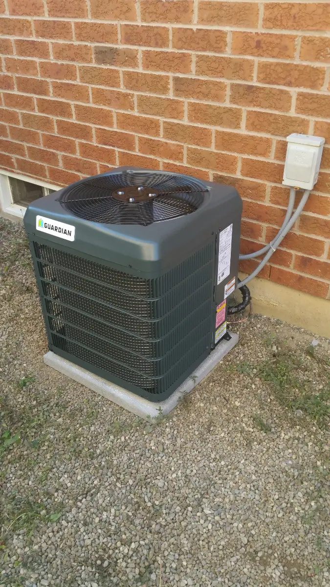 An outdoor air conditioning unit sits on a gravel base beside a brick wall, ready to deliver cool comfort. For residents looking for reliability in unpredictable weather, Mississauga Furnace Repair ensures your system stays in peak condition all year round.