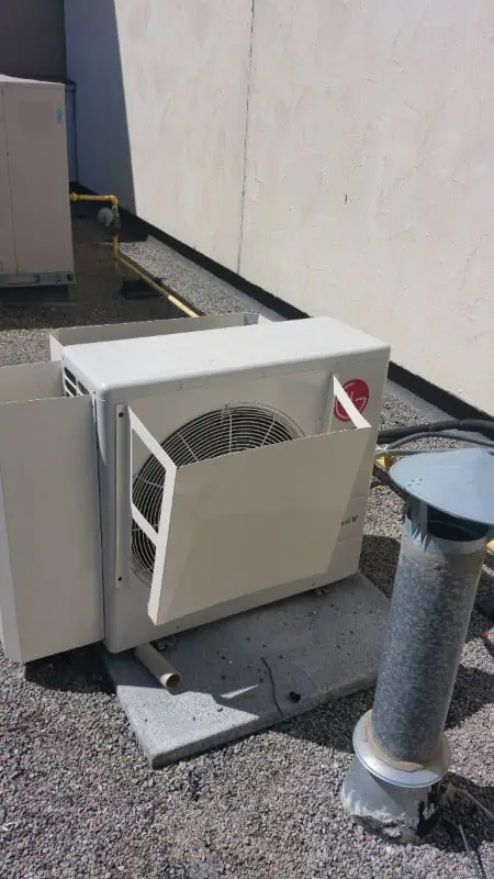 An outdoor air conditioning unit with a detached front panel rests on a gravel rooftop, showcasing the reliable craftsmanship characteristic of HVAC services in Oakville.