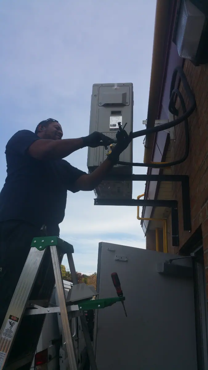 A man on a ladder installs or repairs an HVAC unit on a building exterior in Mississauga.