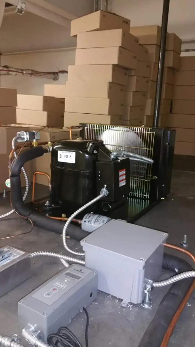 Industrial compressor setup with cables and control boxes in a room, highlighting the precision of HVAC systems. Stacked cardboard boxes create a backdrop in the Oakville facility, underscoring the blend of functionality and organization.