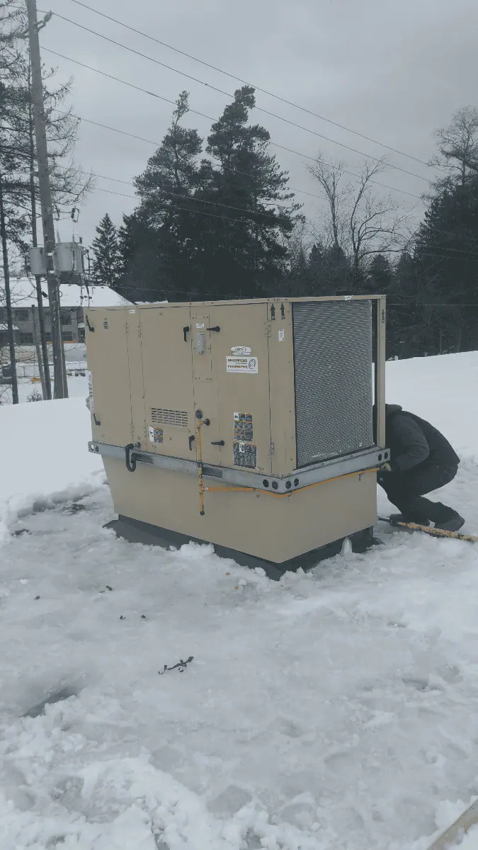 A person is diligently working on a large beige generator amidst a snowy outdoor setting, surrounded by trees and utility poles in the distance. This scene captures the essence of HVAC Oakville's commitment to reliable energy solutions, even in the harshest conditions.