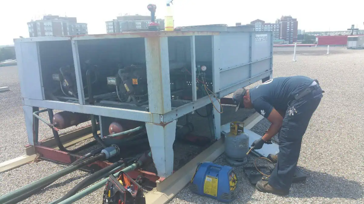 A technician is meticulously inspecting and working on a large rooftop HVAC unit in Mississauga, with tools and equipment nearby under a clear sky.