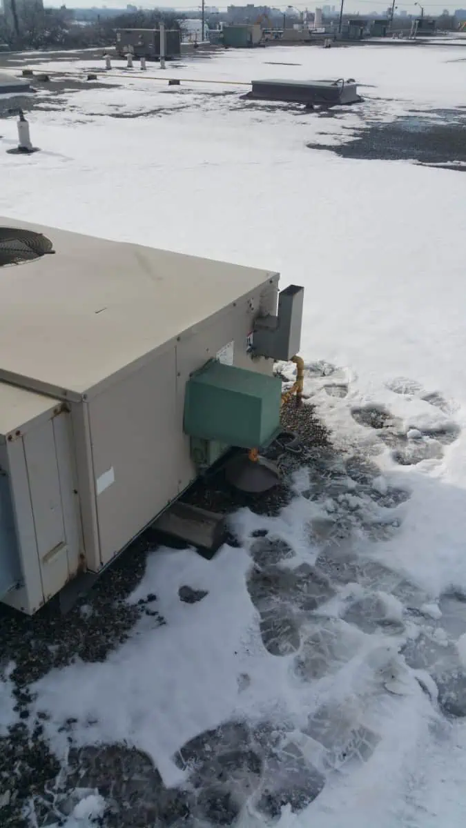 A rooftop in Mississauga with a snow-covered surface and a large HVAC unit, where footprints are visible around the equipment—perhaps left by a technician from a local furnace repair service.