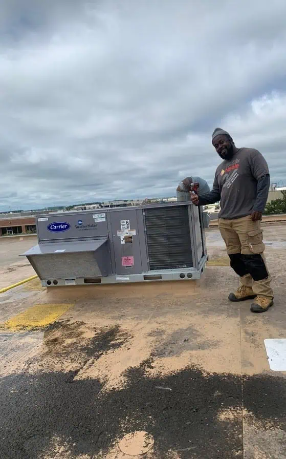 A person stands next to a large HVAC unit on a rooftop under a cloudy sky, expertly maintaining the equipment as part of an HVAC service in Halton Hills.