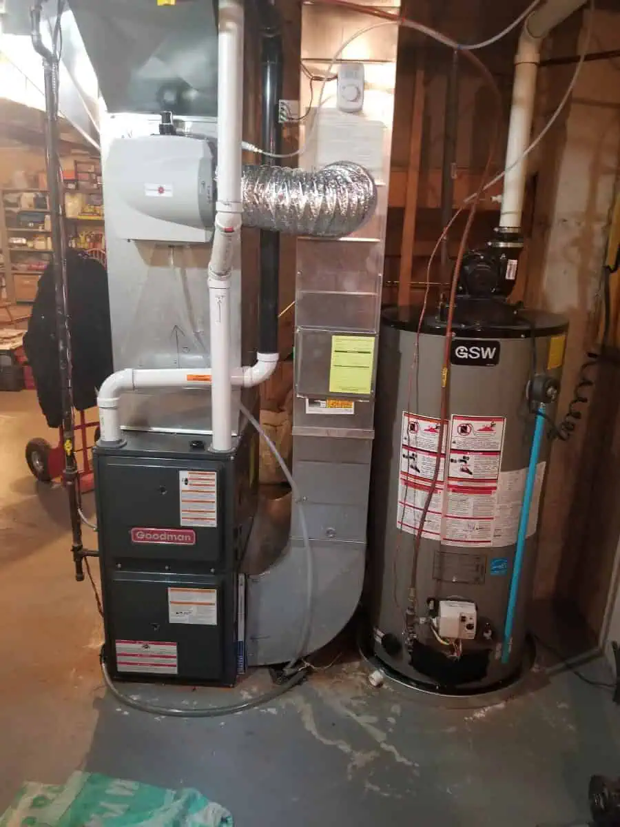 In a Brampton, Canada basement, an impressive layout showcases a furnace and water heater intricately connected by pipes and ductwork. This well-organized space hints at the work of a skilled HVAC contractor, with shelves of tools and boxes neatly arranged in the background.