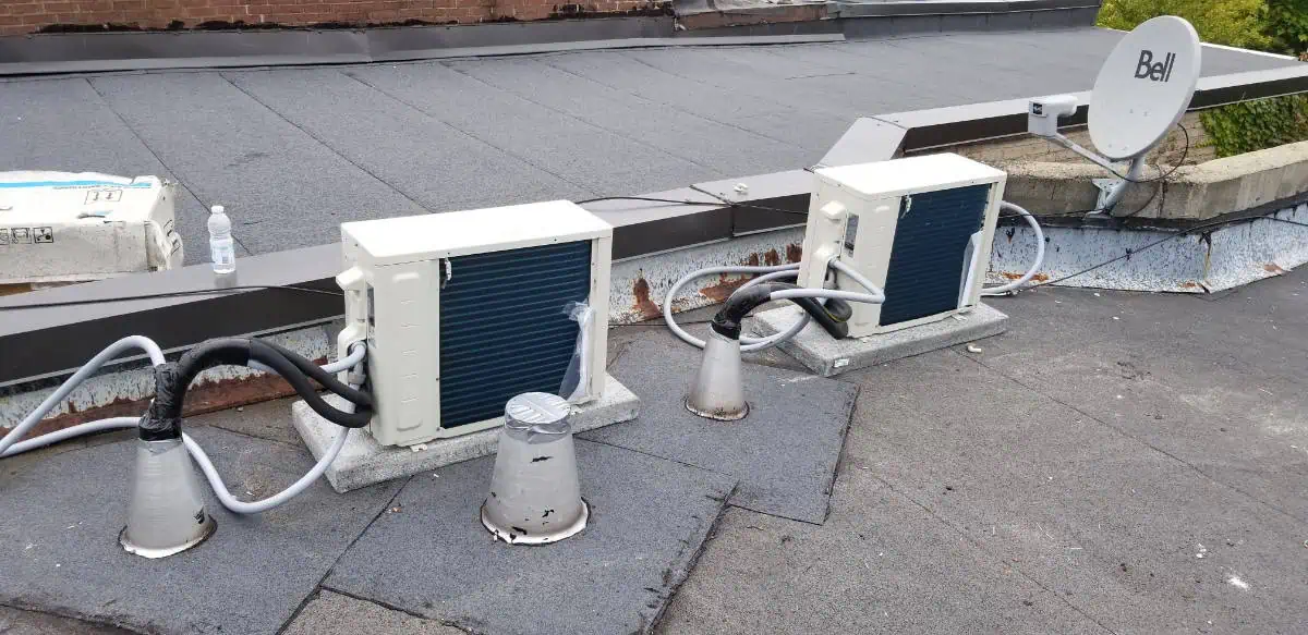 Two air conditioning units and a Bell satellite dish are mounted on a flat rooftop, with wiring and piping visible—a typical setup for efficient HVAC service in Halton Hills.