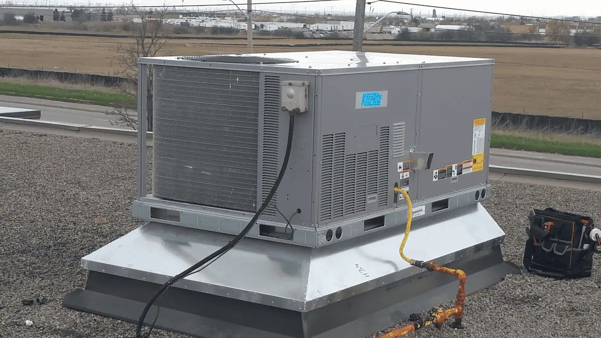 The rooftop HVAC unit sits on a flat surface, with cables and pipes intricately connected, set against an industrial landscape. Perfectly maintained by expert HVAC service in Halton Hills, it stands as a testament to efficiency and reliability.